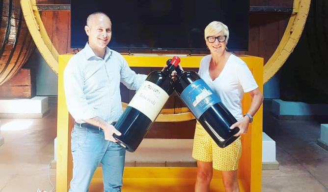 two memebers of the wine reserve team holding giant bottles of wine 