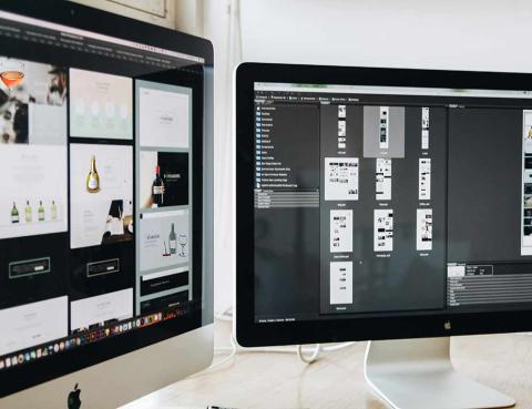 Two monitors on a desk that show website design concepts